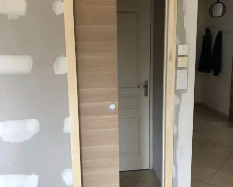 Un habillage en bois posé contre une cloison plaquée, près d’une porte