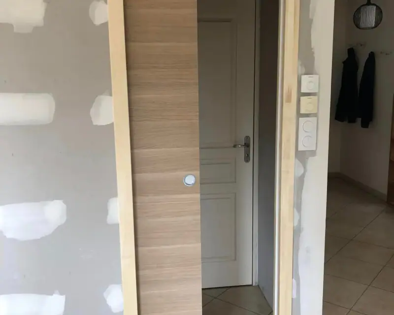 Un habillage en bois posé contre une cloison plaquée, près d’une porte