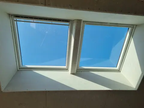 Une double fenêtre de toit habillée de plaques de plâtre, ciel bleu