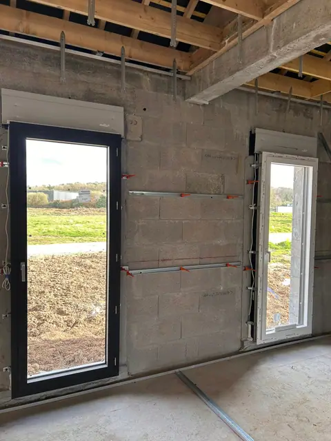 Un mur en parpaings brut avec une porte-fenêtre, les premiers rails posés