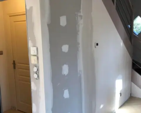 Un mur plaqué le long d’un escalier, bandes et enduit posés, porte à gauche