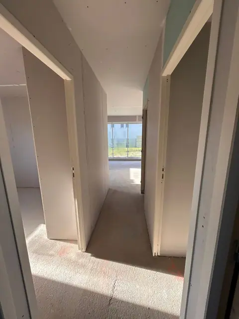 Un couloir plaqué desservant plusieurs chambres, lumière du jour au fond