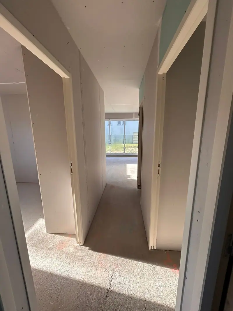 Un couloir plaqué desservant plusieurs chambres, lumière du jour au fond