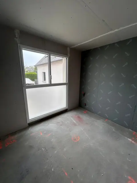 Une chambre aux murs en plaques de plâtre, une fenêtre lumineuse