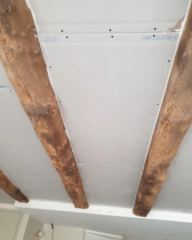 Un plafond en plaques de plâtre posé entre deux poutres anciennes conservées