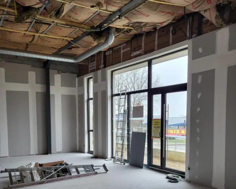 Un local commercial à grande vitrine, murs plaqués et bandes posées, plafond en cours