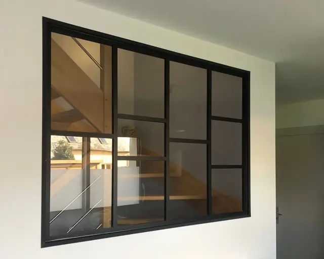 Une verrière intérieure noire à petits carreaux, posée dans une cloison blanche